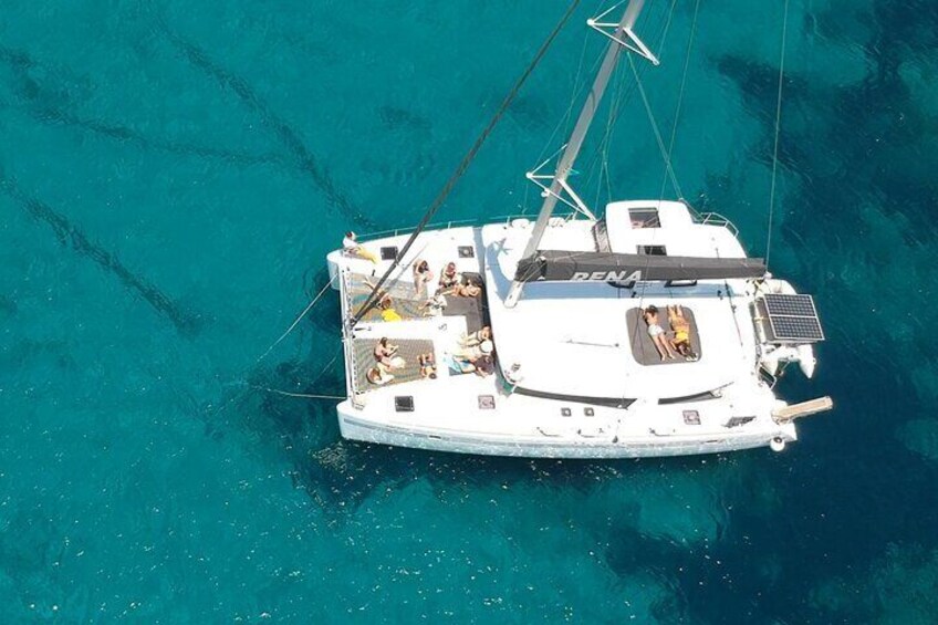 A white yacht named 'RENA' with multiple people on deck, anchored in clear turquoise waters. 5