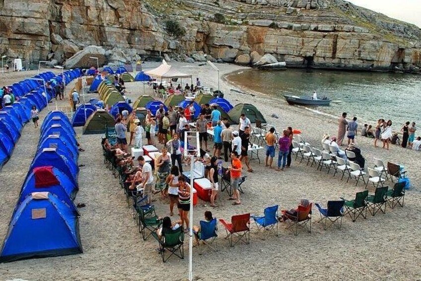 A beach with tents and chairs, people gathered, and a rocky shoreline. 2