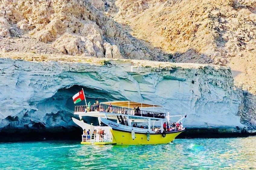 A boat with a flag, passengers, and a rocky cliff in the background. 5