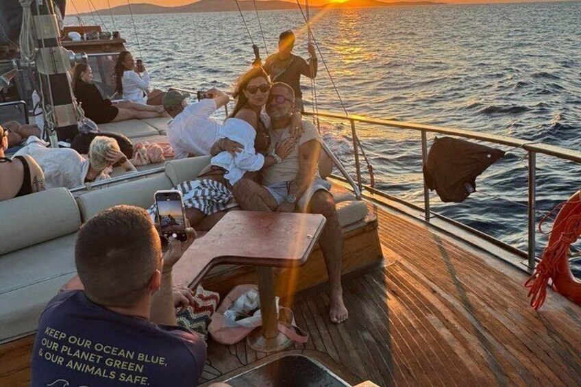 A boat with people sitting on the deck, a sunset in the background, and a person taking a photo. 2