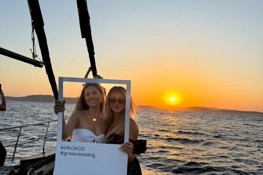Two people on a sailboat at sunset with a clear sky and calm sea. 1