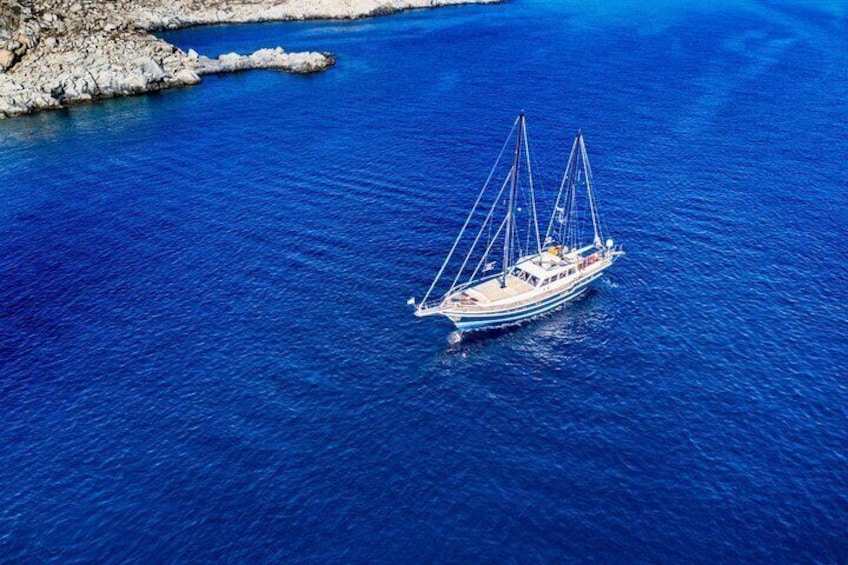 A sailboat on a calm blue sea with rocky coastline. 5