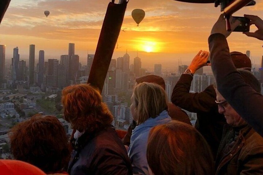 Un groupe de personnes observe un coucher de soleil sur une ville, avec des montgolfières dans le ciel. 4