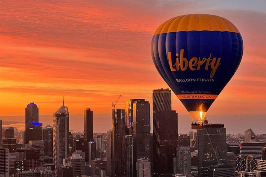 A city skyline at sunset with a hot air balloon labeled 'Liberty Balloon Flights' in the foreground. 3