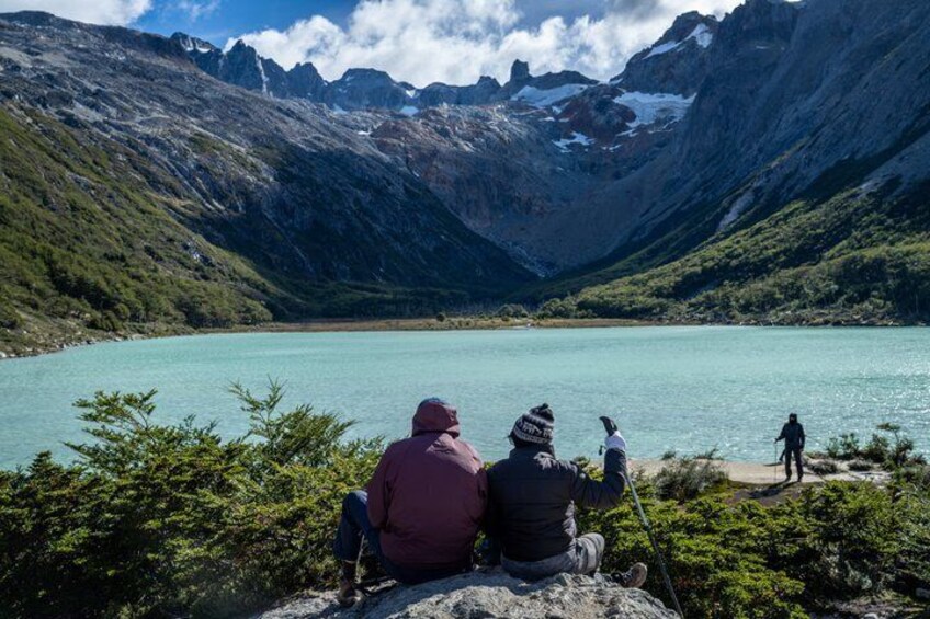 Two people sitting on a rock by a turquoise lake surrounded by mountains. 2