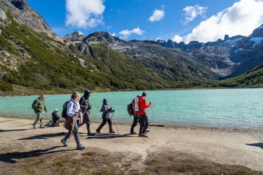 A group of hikers walking along a lakeside path with mountains in the background. 4