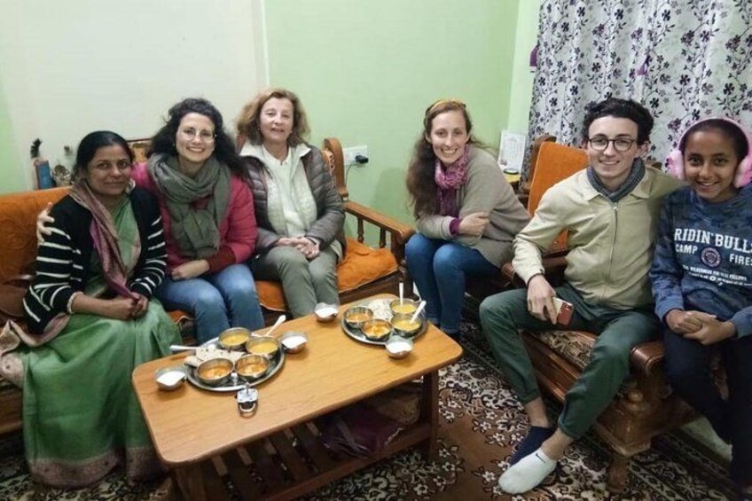A group of people sitting on a couch and chairs around a table with food. 1