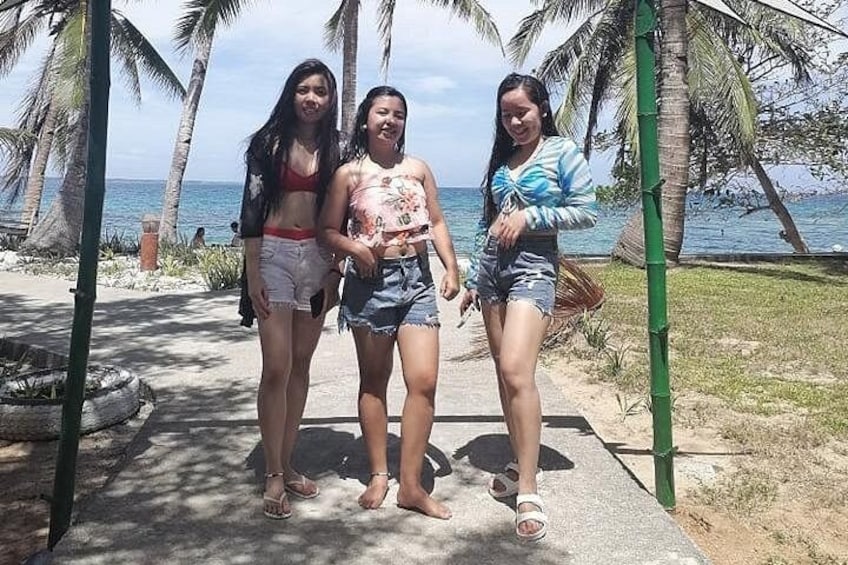 Three people standing on a concrete path with palm trees and a beach in the background. 3