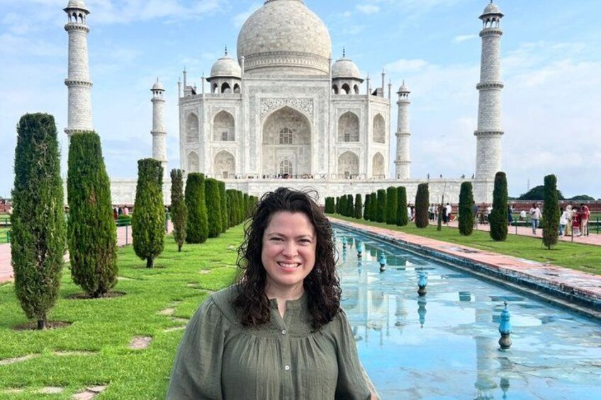 A person standing in front of the Taj Mahal with a pool and neatly trimmed trees. 1