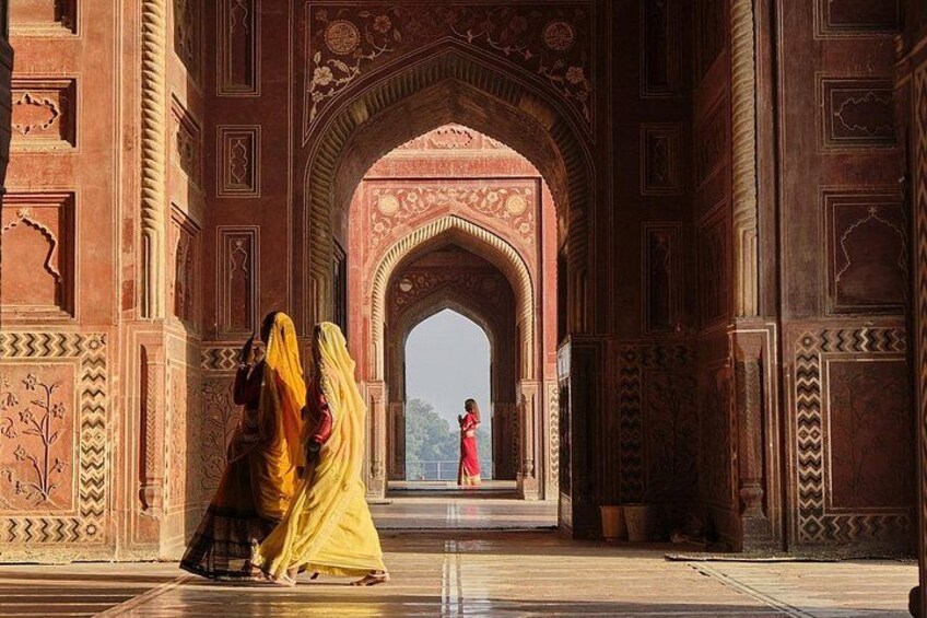 An ornate archway with intricate designs, a tiled floor, and a person in a red dress standing in the distance. 2