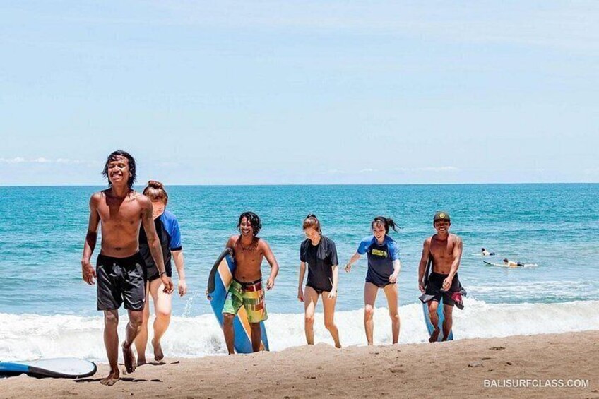 A group of people on a beach with surfboards, ocean waves, and a clear sky. 3