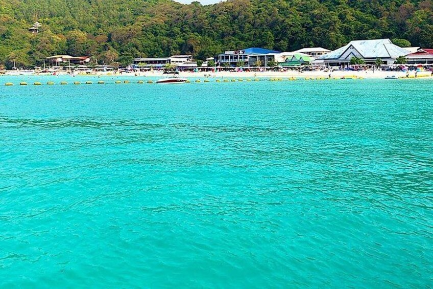 A turquoise sea, a beach with people, and buildings in the background. 2
