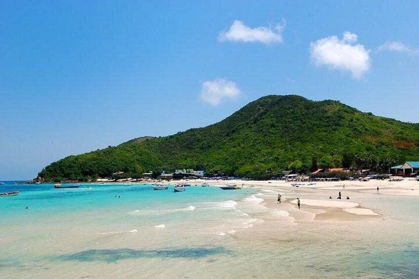 A beach with clear turquoise water, a sandy shore, and a green hill in the background. 5