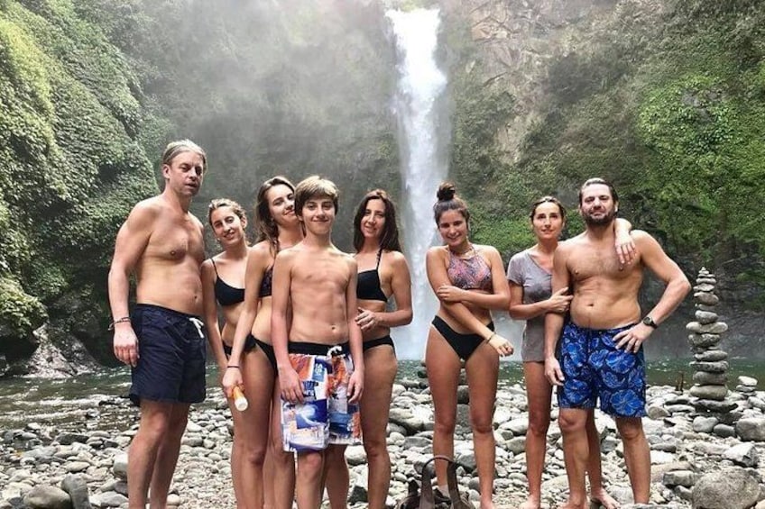 A group of people standing in front of a waterfall with a rocky riverbed. 2