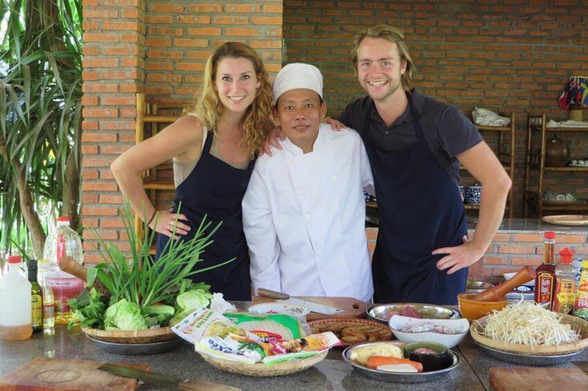 Three people standing in front of a table with various food items and cooking utensils. 1