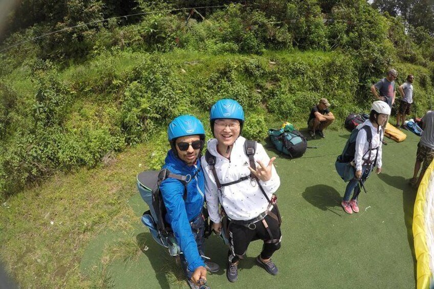 Two people wearing helmets and backpacks, standing on a green surface with greenery in the background. 1