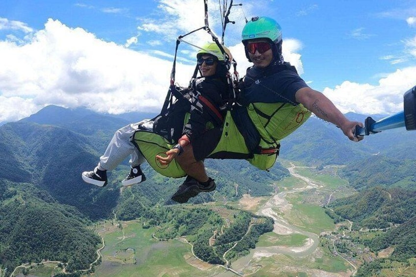 Two people paragliding over a mountainous landscape with a river below. 2