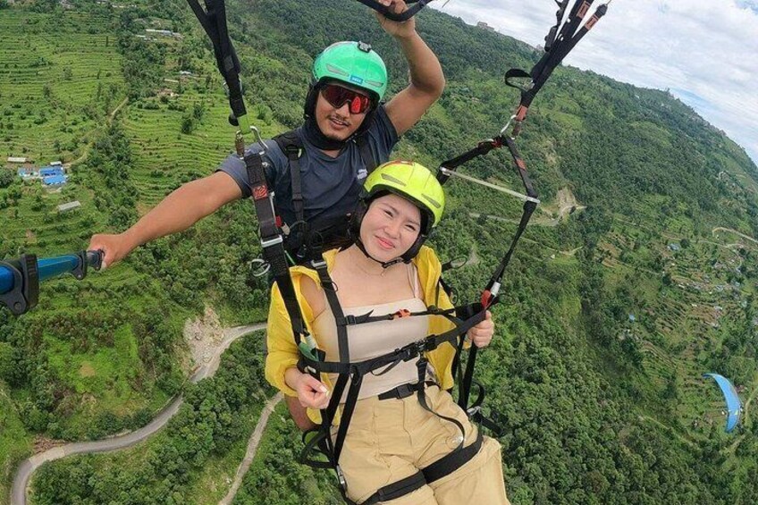 Two people skydiving with parachutes over a lush green landscape. 3