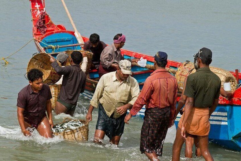 People wading in water, some carrying baskets, near a red and blue boat. 3