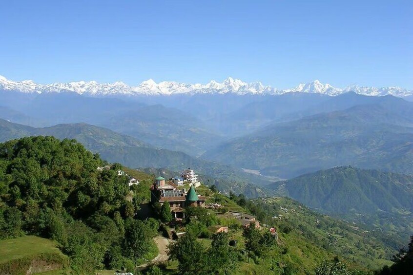 A mountainous landscape with snow-capped peaks in the background, lush green valleys, and a small cluster of buildings with green roofs. 2