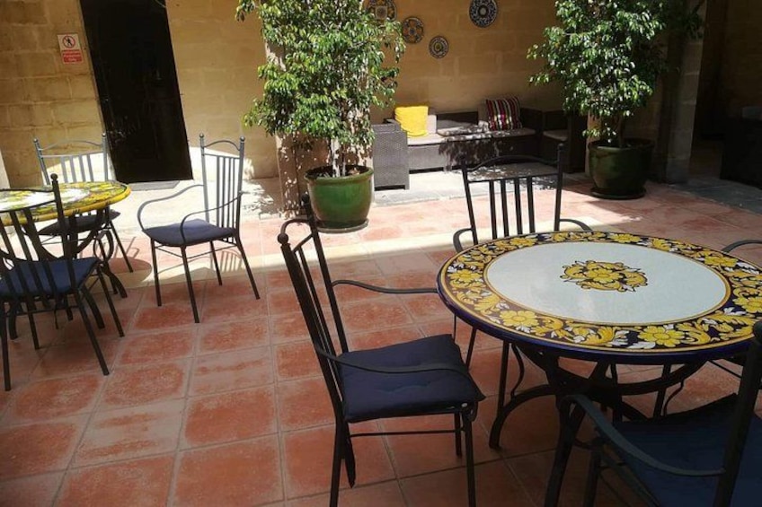 Un patio al aire libre con suelo de baldosas, mesas redondas con sillas y plantas en macetas. 4
