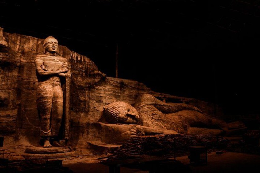 A large stone statue of a seated figure with arms crossed, set against a rocky backdrop. 4