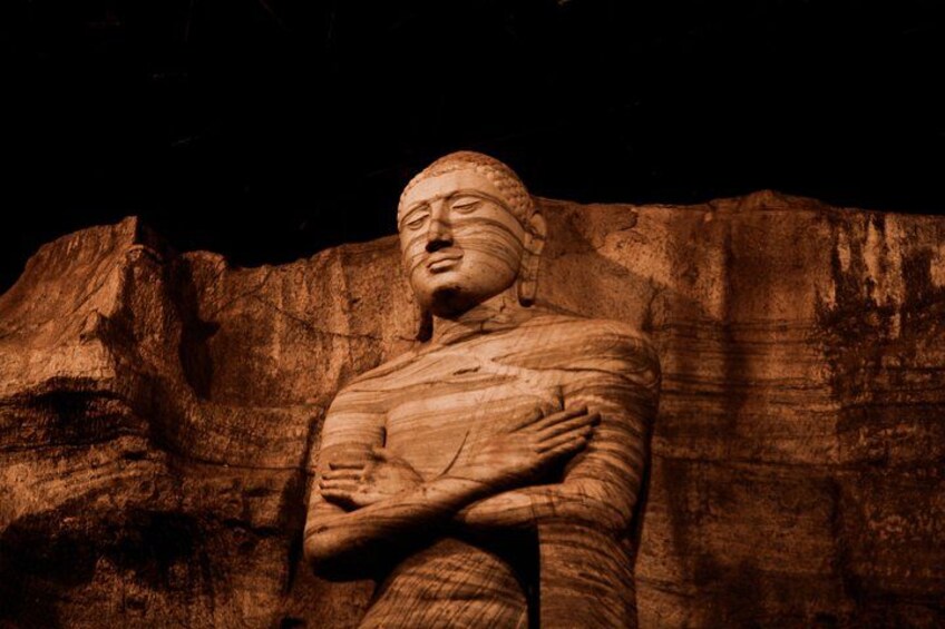 A large stone statue with arms crossed, set against a rocky background. 3