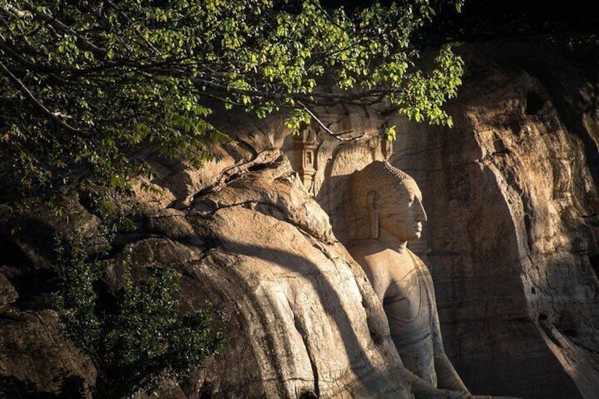 Un'imponente statua in pietra raffigura una figura seduta, parzialmente nascosta dalla vegetazione, con una scogliera rocciosa sullo sfondo. 3