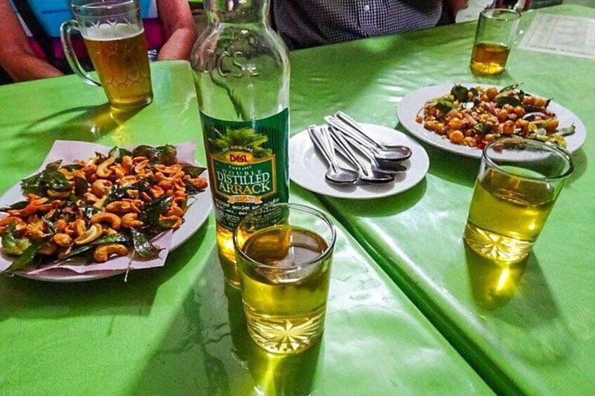 A table with a bottle of Distilled Arrack, plates of food, and glasses of beer. 2