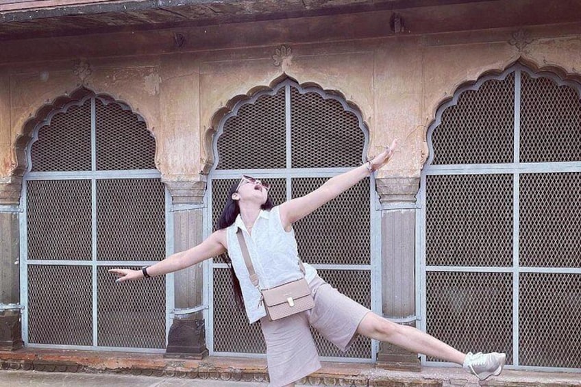 A person performing a dance in front of a building with ornate arches and lattice windows. 5