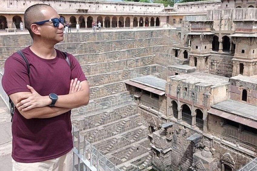 A man standing in front of a large, ancient stone structure with multiple levels and arched openings. 1