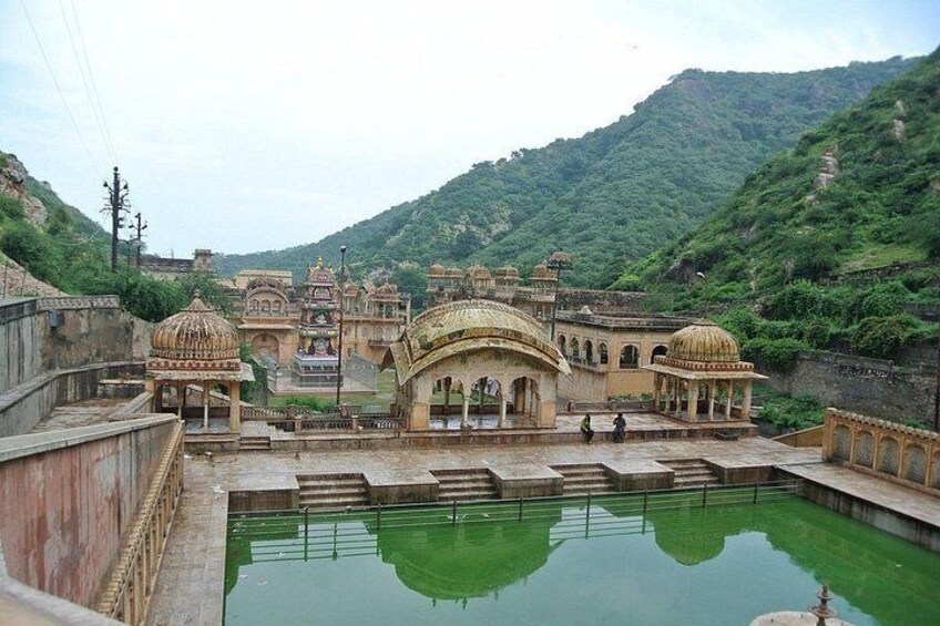 A historical building complex with domed structures and a central pavilion, surrounded by a water body and hilly terrain. 2