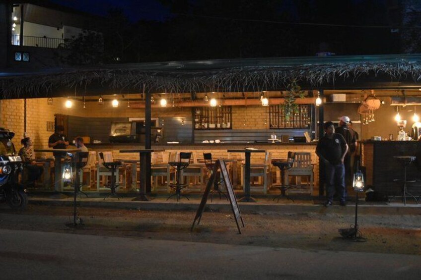 An outdoor bar with tables and chairs, a thatched roof, and a brick wall. 3