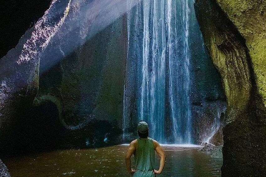 A person standing in front of a waterfall in a cave. 3