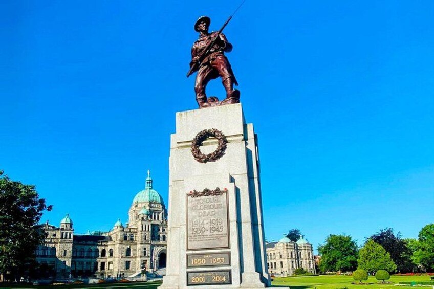 Una estatua de un soldado sobre un pedestal con una corona y una placa. Al fondo, un edificio grande con una cúpula. 4