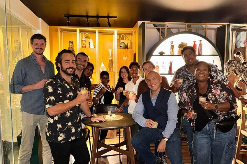 A group of people at a social gathering in a room with shelves of bottles and a round table. 3