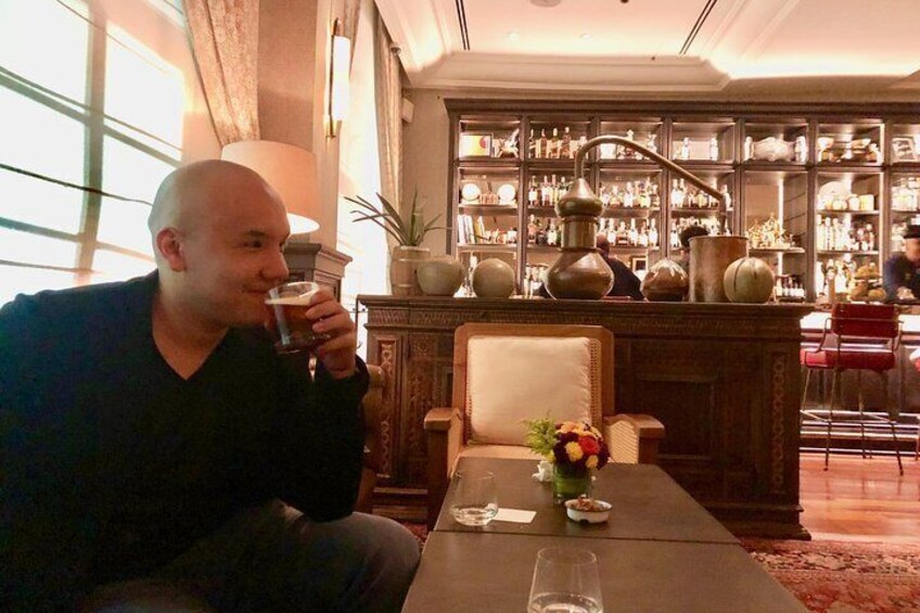 A man seated at a table in a room with a bar in the background. 1