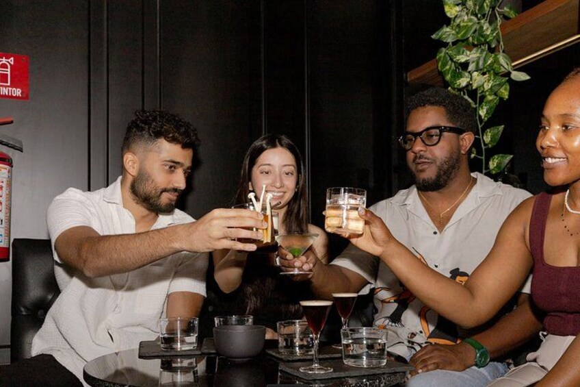 A group of people toasting with drinks at a table with glasses and a bowl. 1
