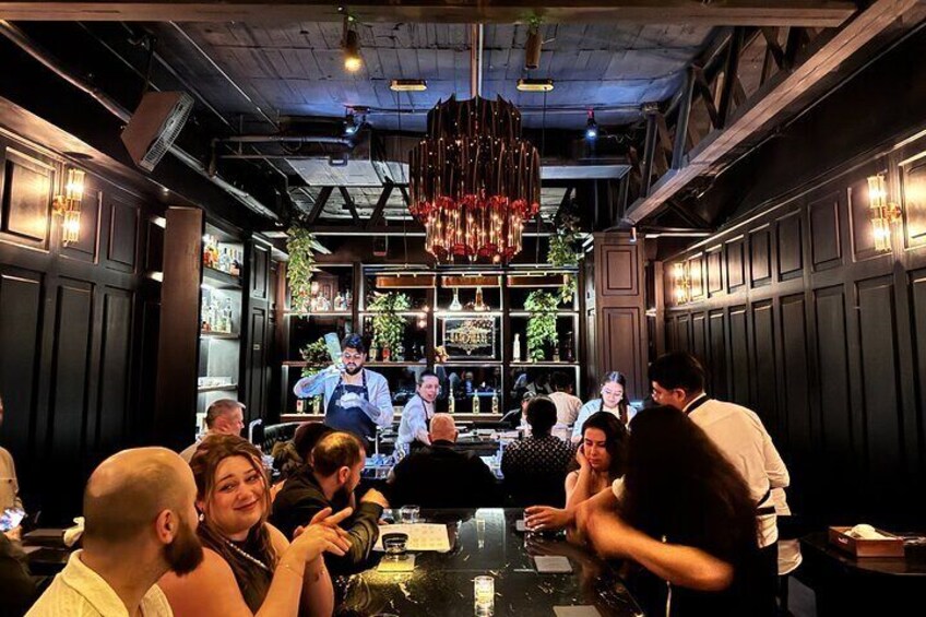 A bar with patrons seated at tables, a bartender at the counter, and a well-stocked bar area in the background. 4