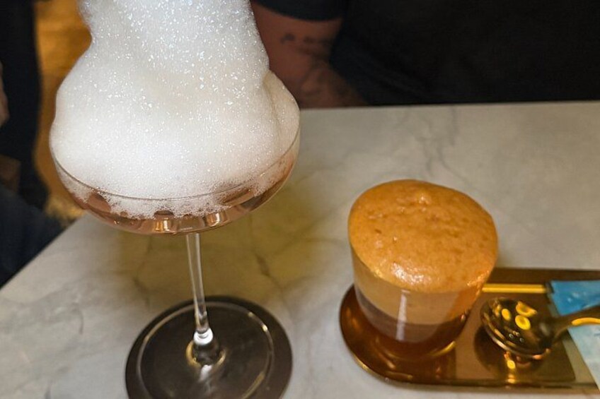 A glass with a foamy beverage and a round, golden-brown object on a tray. 2
