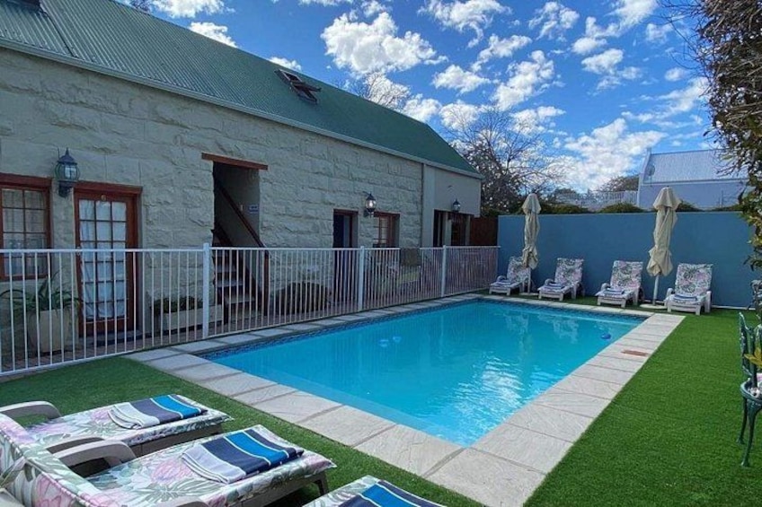 A swimming pool with lounge chairs, a white fence, and a building with a green roof. 4