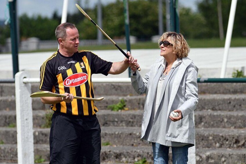 A person in a striped shirt holding a stick and a ball, and another person in a light jacket. 1