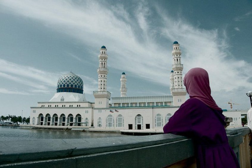 A mosque with a large dome and two minarets, a person in a purple hijab, and a cloudy sky. 4