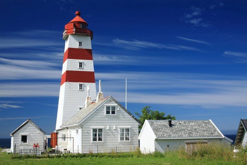 A lighthouse with a red and white striped tower, a small white building with a grey roof, and a grassy foreground. 3