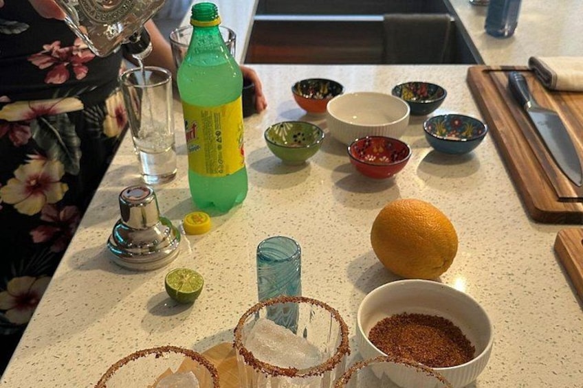 Una encimera de cocina con varios objetos, incluyendo una botella de refresco verde, una lima, un vaso, un cuenco de especias y un cuchillo sobre una tabla de cortar. 4