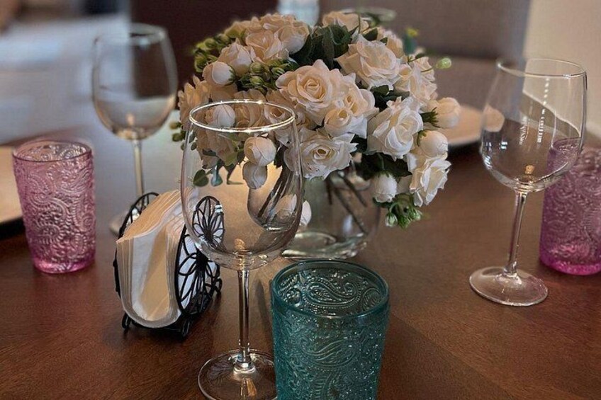Una mesa con un jarrón de rosas blancas, copas de vino y cristalería decorativa. 2