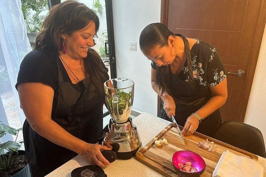 Dos personas preparando comida, una usando una licuadora y la otra picando verduras. 1