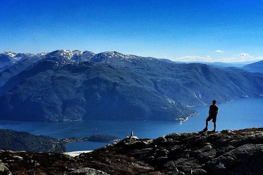 Una persona de pie sobre un saliente rocoso con vista a un lago y montañas. 1