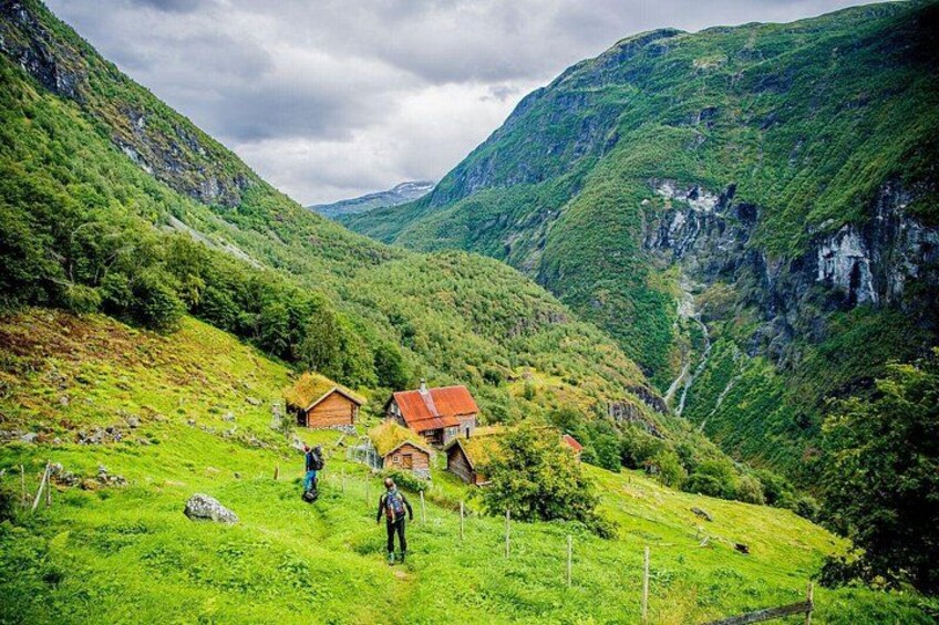 Paisaje montañoso con colinas verdes, algunas casas con techos rojos y una persona caminando. 2