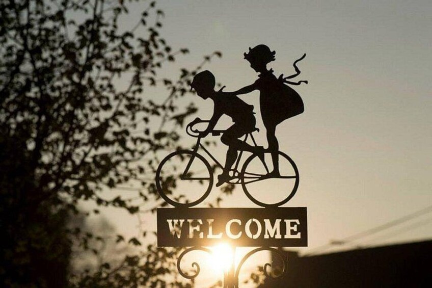A silhouette of a child and an adult on a bicycle with a 'WELCOME' sign. 1